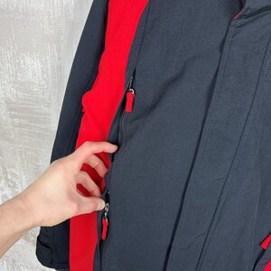 May include: Black and red winter jacket with a high collar and zippered pockets. The jacket features red accents on the sides and a zipper closure. The jacket is made of a durable material, suitable for cold weather.