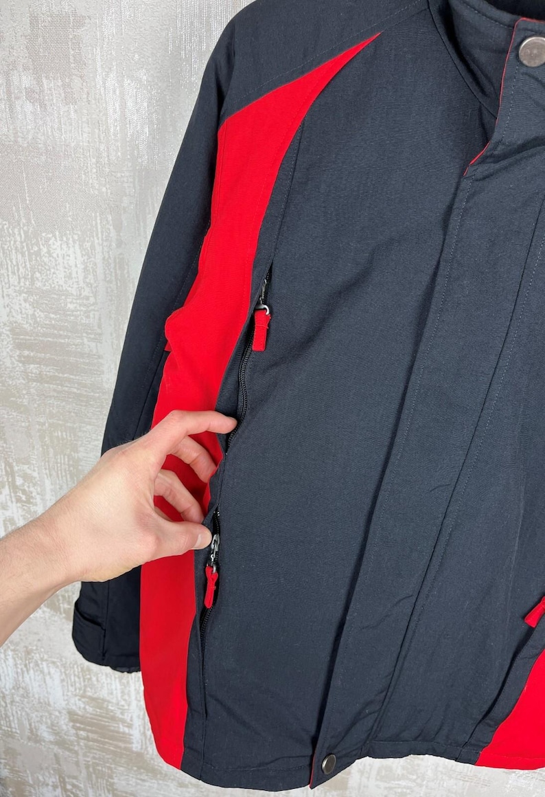 May include: Black and red winter jacket with a high collar and zippered pockets. The jacket features red accents on the sides and a zipper closure. The jacket is made of a durable material, suitable for cold weather.