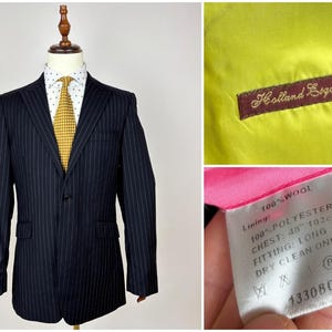May include: Navy blue pinstripe suit jacket on a mannequin, paired with a white shirt and yellow tie. The jacket has a two-button closure and a chest measurement of 40 inches. The lining is yellow with a "Holland Esquire" label.