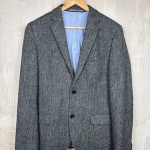 Puede incluir: Una taza de cerámica blanca con un asa negra y el texto "But First, Coffee" en negrita negra. La taza está llena de un líquido oscuro, probablemente café, y se encuentra sobre una superficie clara.