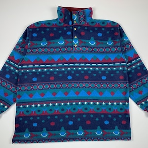 May include: A blue, green, red and white patterned fleece pullover with a mock neck and a single button closure.