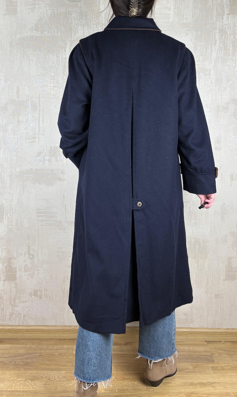 May include: A long navy blue coat with a brown trim around the collar and cuffs. The coat has a single button closure at the back.