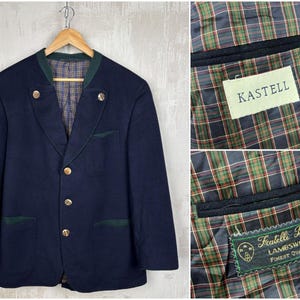 May include: A navy blue blazer with gold buttons and green trim, featuring a plaid lining. The jacket has a classic design with a notched collar and two front pockets. The interior includes Kastell and Fratelli Bacci labels.