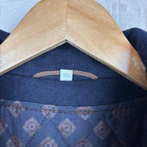 May include: Close-up of the inside of a navy blue jacket with a brown quilted lining. The lining has a repeating pattern of small, stylized flowers. A brown tag with the number "20" is sewn into the lining.