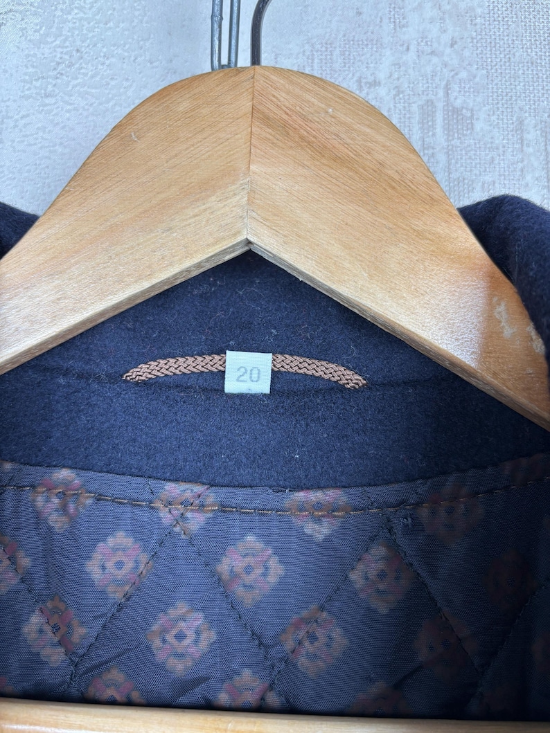 May include: Close-up of the inside of a navy blue jacket with a brown quilted lining. The lining has a repeating pattern of small, stylized flowers. A brown tag with the number "20" is sewn into the lining.