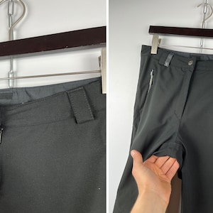 May include: Dark gray pants with a zipper and button closure. The pants have two zippered pockets on the sides.