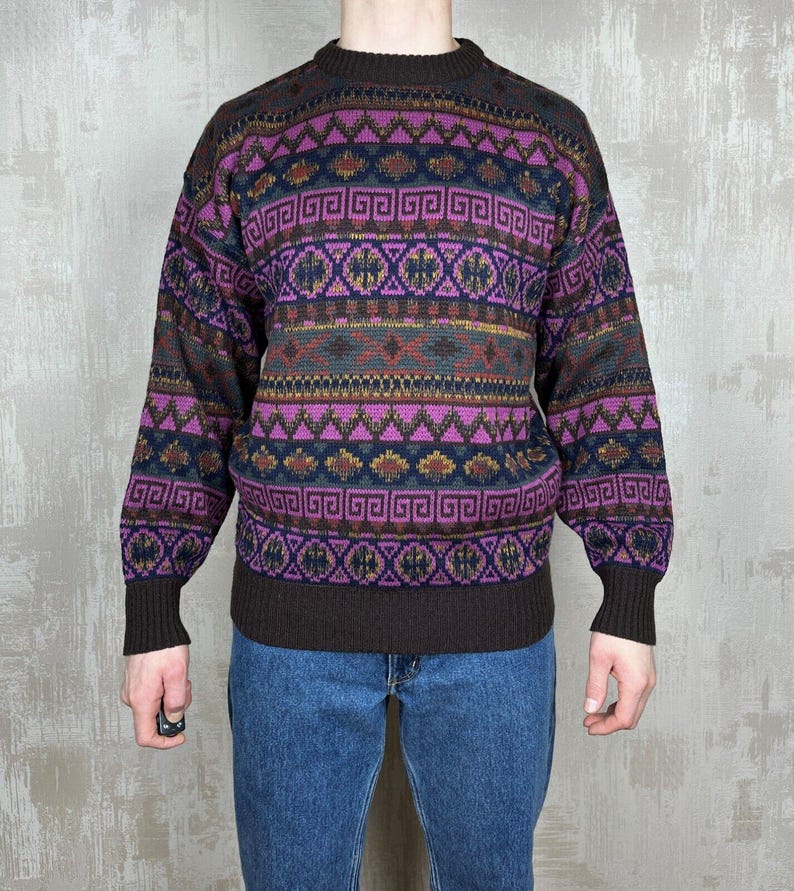 K&ouml;nnte beinhalten: Ein Vintage-Pullover mit geometrischem Muster in Lila, Braun und Gr&uuml;n. Der Pullover hat einen Rundhalsausschnitt und lange &Auml;rmel. Das Design zeigt sich wiederholende Formen und Linien.