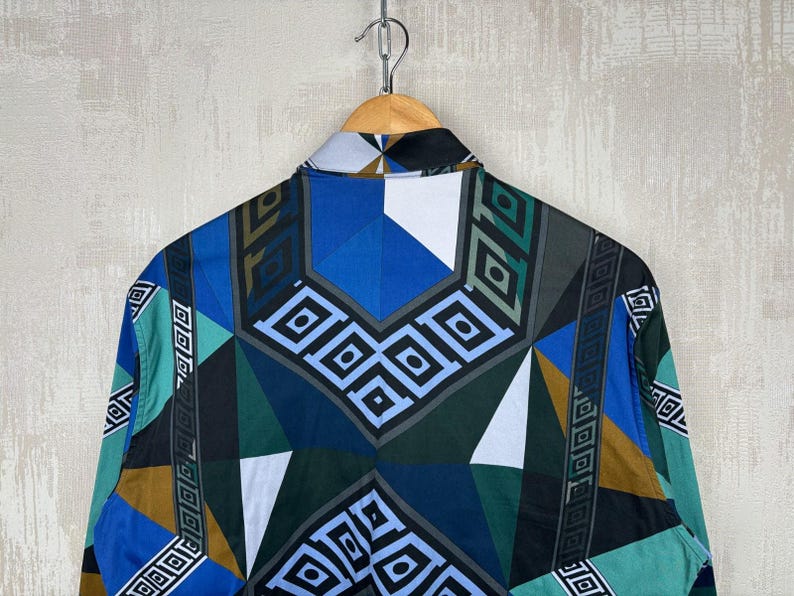 May include: A patterned button-down shirt in blue, teal, brown, and black. The geometric design features diamond and rectangular shapes. The shirt is hanging from a wooden hanger.