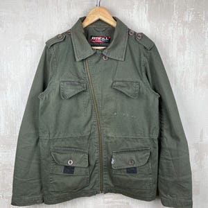 May include: Olive green jacket with a zipper closure, multiple pockets, and button details. The jacket has a collared neckline and epaulettes. The brand name "O'Neill" is visible on a label. The jacket is hanging on a wooden hanger.