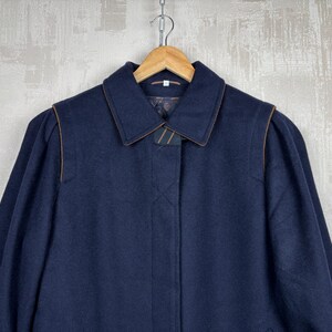 May include: A navy blue wool coat with a brown trim around the collar and pockets. The coat has a long sleeve and a button closure.