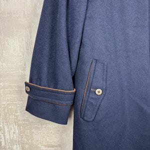 May include: A navy blue wool coat with brown trim around the cuffs and pockets. The coat has a single button on the cuff and two buttons on the pocket flap.