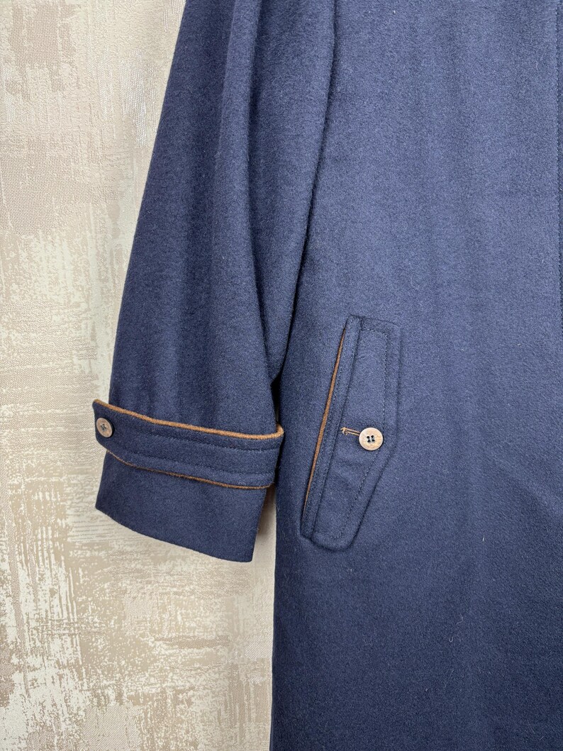 May include: A navy blue wool coat with brown trim around the cuffs and pockets. The coat has a single button on the cuff and two buttons on the pocket flap.