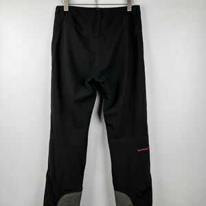May include: Black hiking pants with a red Mammut logo on the right leg. The pants have a grey panel on the lower legs.