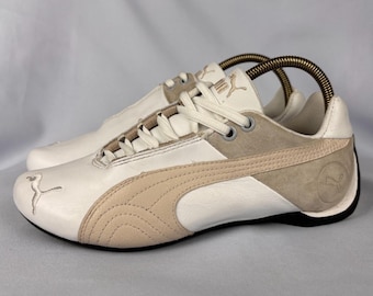 May include: Pair of Puma sneakers in white, beige, and gray. The shoes feature a leather upper with suede accents and a black sole. The Puma logo is visible on the side and tongue. The sneakers are designed for casual wear.