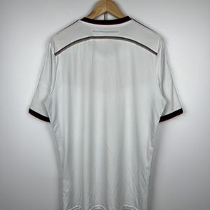 May include: White soccer jersey with black and red trim. The text "DIE NATIONALMANNSCHAFT" is printed on the back of the jersey.