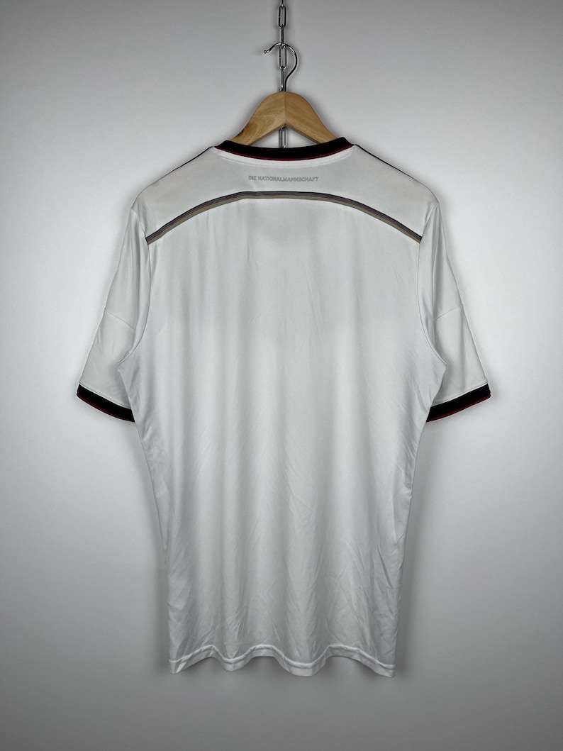 May include: White soccer jersey with black and red trim. The text "DIE NATIONALMANNSCHAFT" is printed on the back of the jersey.