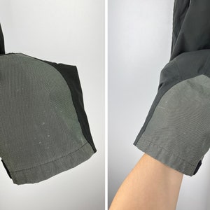 May include: Close-up of black pants with gray reinforced knee patches. The pants are made of a lightweight, water-resistant fabric.