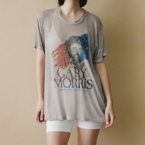 May include: A grey, semi-sheer t-shirt with a faded image of Gary Morris, a singer, and the text "Gary Morris Back from Broadway".