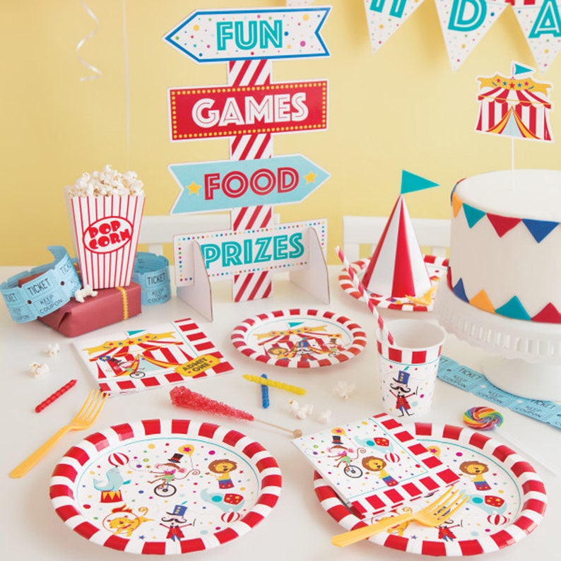 K&ouml;nnte beinhalten: Ein Zirkus-Partyset mit rot-wei&szlig; gestreiften Papptellern, Servietten und Bechern. Das Set enth&auml;lt au&szlig;erdem eine Popcorn-Box, eine Torte und ein Schild mit der Aufschrift "Fun, Games, Food, Prizes".