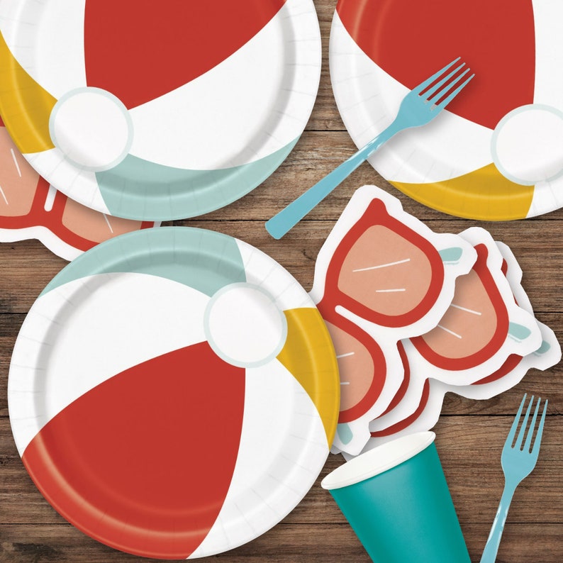 Puede incluir: Suministros para fiestas con tem&aacute;tica de playa, que incluyen platos de papel, recortes con forma de gafas de sol, una taza turquesa y tenedores. Los platos presentan secciones rojas, amarillas, blancas y azules. Dispuestos sobre una superficie de madera.