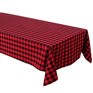 May include: A red and black buffalo check tablecloth. The tablecloth is rectangular and has a classic plaid pattern. The fabric is folded over the edge of a table, showcasing the pattern and texture of the material.