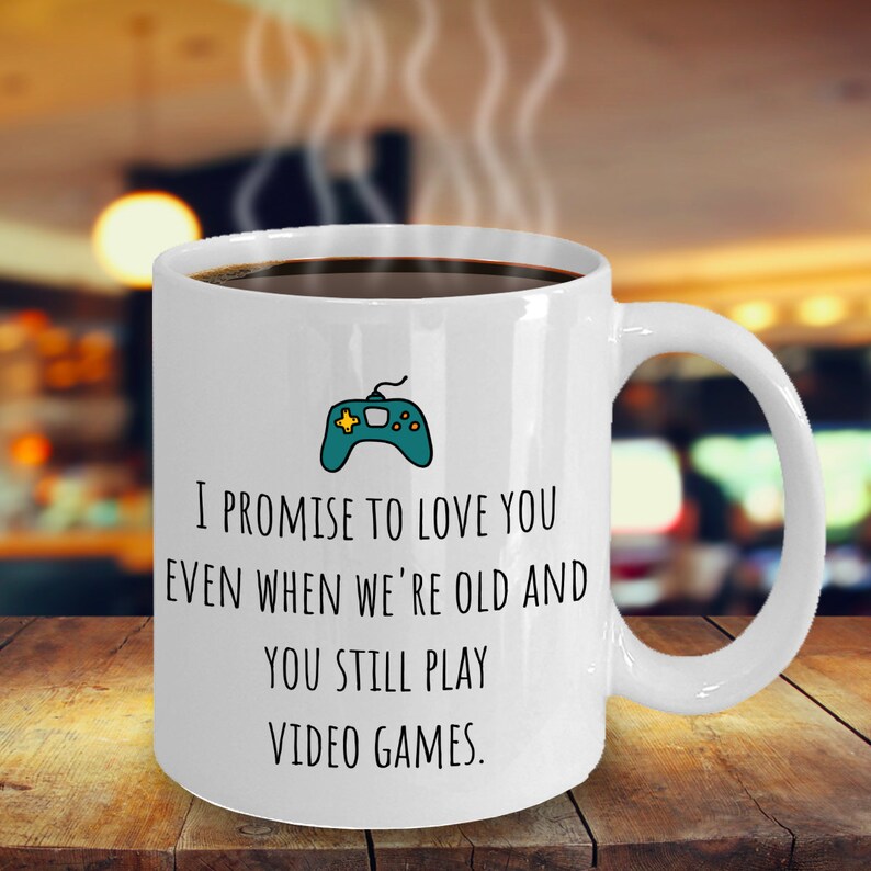May include: White coffee mug with a green video game controller graphic and the text "I promise to love you even when we're old and you still play video games."