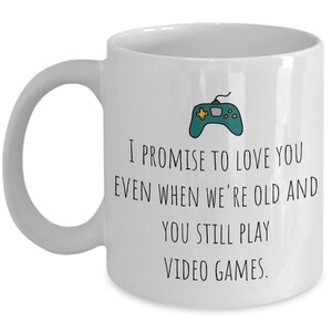May include: White ceramic coffee mug with a black and green video game controller graphic and the text "I promise to love you even when we're old and you still play video games."