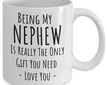May include: White ceramic mug with the text "Being My Nephew Is Really The Only Gift You Need - Love You -" in black. The mug has a curved handle and is designed for hot beverages.