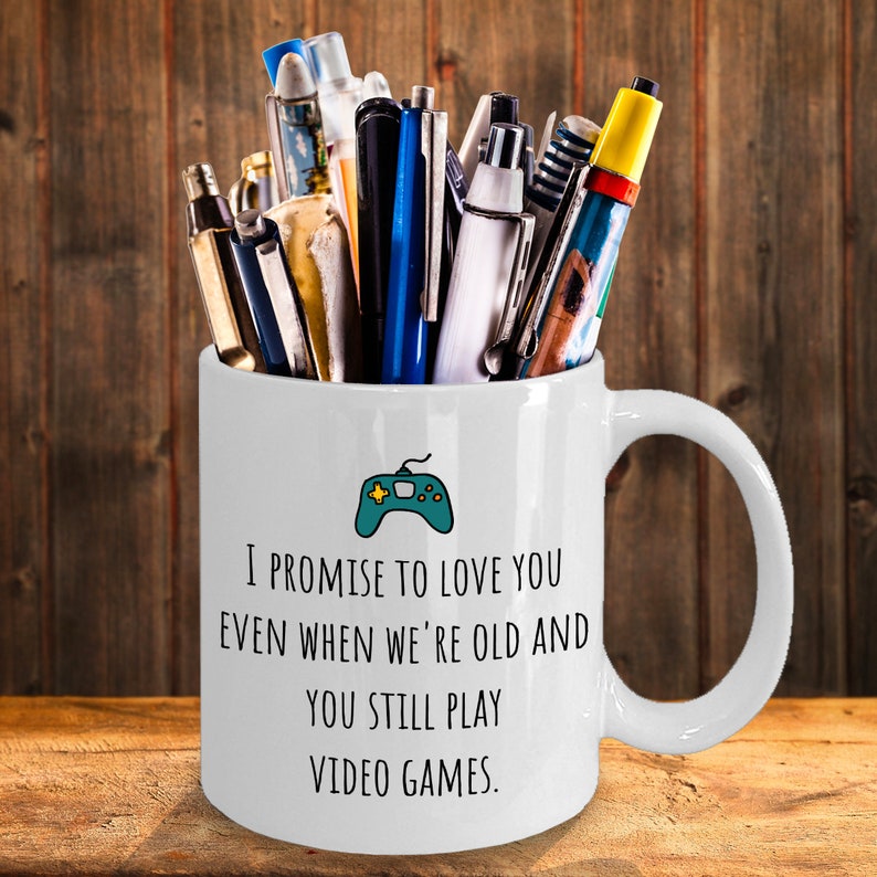 May include: White ceramic coffee mug with a green video game controller graphic and the text "I promise to love you even when we're old and you still play video games."