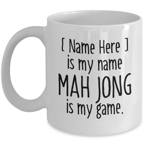 May include: White ceramic coffee mug with black text that reads "[ Name Here ] is my name MAH JONG is my game."