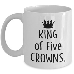 May include: White ceramic mug with a black crown and the text "King of Five Crowns."