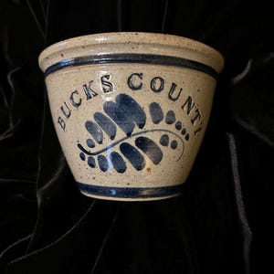 May include: A cream-colored ceramic bowl with a blue rim and a blue design of a leaf with the words "Bucks County" written around it.