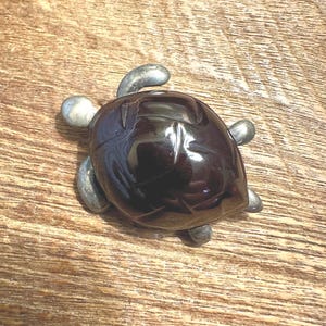 May include: A dark brown turtle figurine with a silver metal shell and legs. The turtle is sitting on a wooden surface.