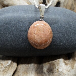 May include: A silver chain necklace with a pendant made from a smooth, light brown stone. The stone has a slightly marbled appearance.