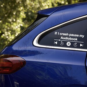 May include: A blue car with a white decal on the rear window. The decal reads "If I crash pause my Audiobook" with media control icons. The car's taillight is red, and the background is blurred green.