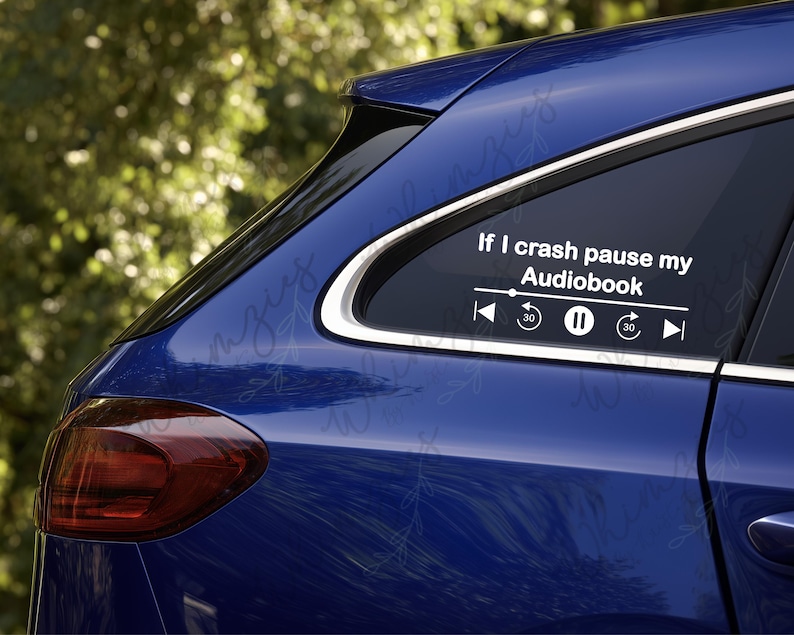 May include: A blue car with a white decal on the rear window. The decal reads "If I crash pause my Audiobook" with media control icons. The car's taillight is red, and the background is blurred green.