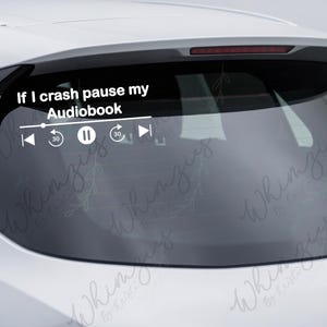 May include: White vinyl car decal with the text "If I crash pause my Audiobook" and media player controls. The decal includes a play/pause button, rewind, and fast forward icons. The decal is applied to a car's rear window.