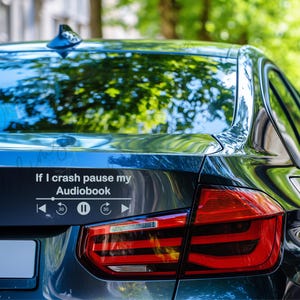 May include: A black car's rear with a white decal that reads "If I crash pause my Audiobook" above a media player interface. The car's taillight is red and the background is blurred green.