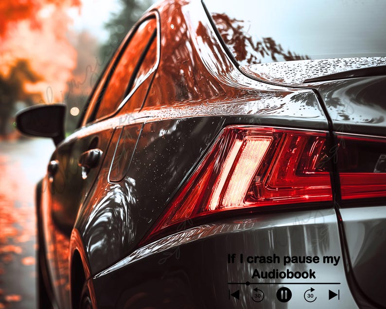 May include: Close-up of a dark gray car's rear, with a red taillight and the text "If I crash pause my Audiobook" with a media player graphic. The car is wet, reflecting the surrounding autumn foliage.