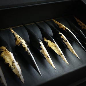 May include: A set of eight black, pointed, decorative objects with gold leaf accents. The objects are arranged in a row in a black box.