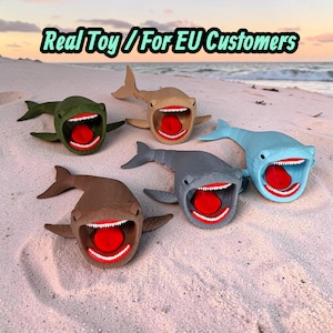 Op de afbeelding: Vijf beweegbare haaienspeeltjes in olijfgroen, beige, bruin, grijs en lichtblauw, elk met een open mond, witte tanden en een rode tong. De tekst "Real Toy / For EU Customers" staat bovenaan de afbeelding.