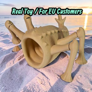 Peut inclure: Un jouet créature beige à plusieurs pattes avec un corps cylindrique creux et ouvert, doté d'une crête dorsale texturée et épineuse. L'objet possède des membres articulés et porte le texte Real Toy / For EU Customers en haut.