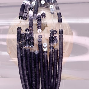 Peut inclure: Un brin de paillettes noires et argentées, enfilées sur un fil fin. Les paillettes sont rondes et plates, et elles sont disposées en un motif répétitif.