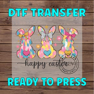 May include: Three colorful bunny silhouettes with a "happy easter" text and "DTF TRANSFER READY TO PRESS" text. The bunnies are in a bright, abstract pattern with pink, blue, and yellow colors.