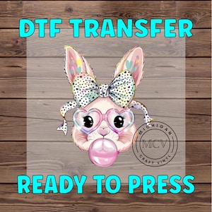 May include: A pink bunny rabbit with a rainbow bow and heart-shaped glasses is blowing a pink bubble. The image is labeled "DTF TRANSFER READY TO PRESS" and "MICHIGAN MCV CRAFT VINYL".