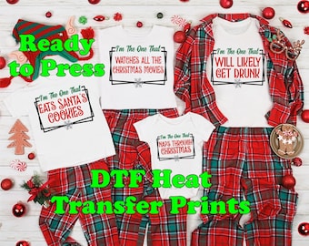 May include: Three white t-shirts with red and green text on a red and green plaid background. The text on the shirts reads "I'm the one that eats Santa's cookies", "I'm the one that watches all the Christmas movies", and "I'm the one that will likely get drunk". The text "DTF Heat Transfer Prints" is written in green on a white background.