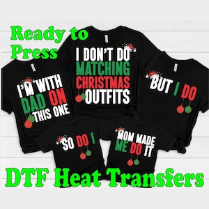 May include: Four black t-shirts with Christmas-themed text and graphics. The shirts read "I'm with Dad on this one", "I don't do matching Christmas outfits", "But I do", and "So do I". The shirts also feature a Santa hat and red and green ornaments.