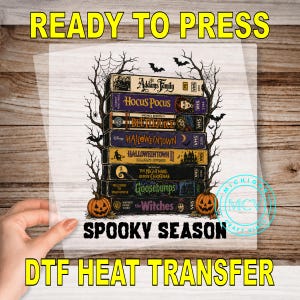 May include: A DTF heat transfer sheet featuring a stack of seven vintage VHS tapes with Halloween-themed movie titles including The Addams Family, Hocus Pocus, and Beetlejuice, framed by bare trees, spiderwebs, bats, and two orange pumpkins.