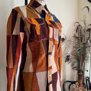 Pode incluir: Uma camisa de camur&ccedil;a em patchwork com fecho de bot&otilde;es e mangas compridas. A camisa &eacute; feita de diferentes pe&ccedil;as de camur&ccedil;a de cores diferentes, incluindo castanho, bege e laranja. A camisa tem um colarinho e um bolso no peito esquerdo.