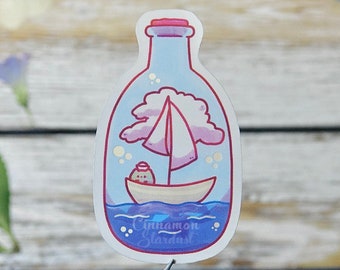 May include: A whimsical sticker featuring a sailboat inside a bottle. The design includes a pink-sailed boat on blue water, a pink cloud, and a small character. The sticker has the text "Cinnamon Stardust" at the bottom.